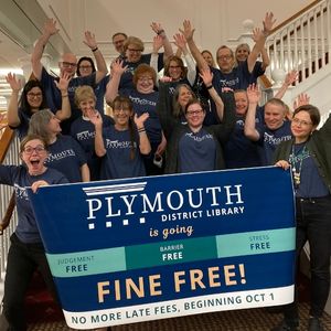 Library staff raise hands in celebration with banner announcing Fine-Free status